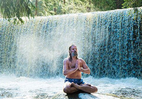 Man meditating in front of waterfall.